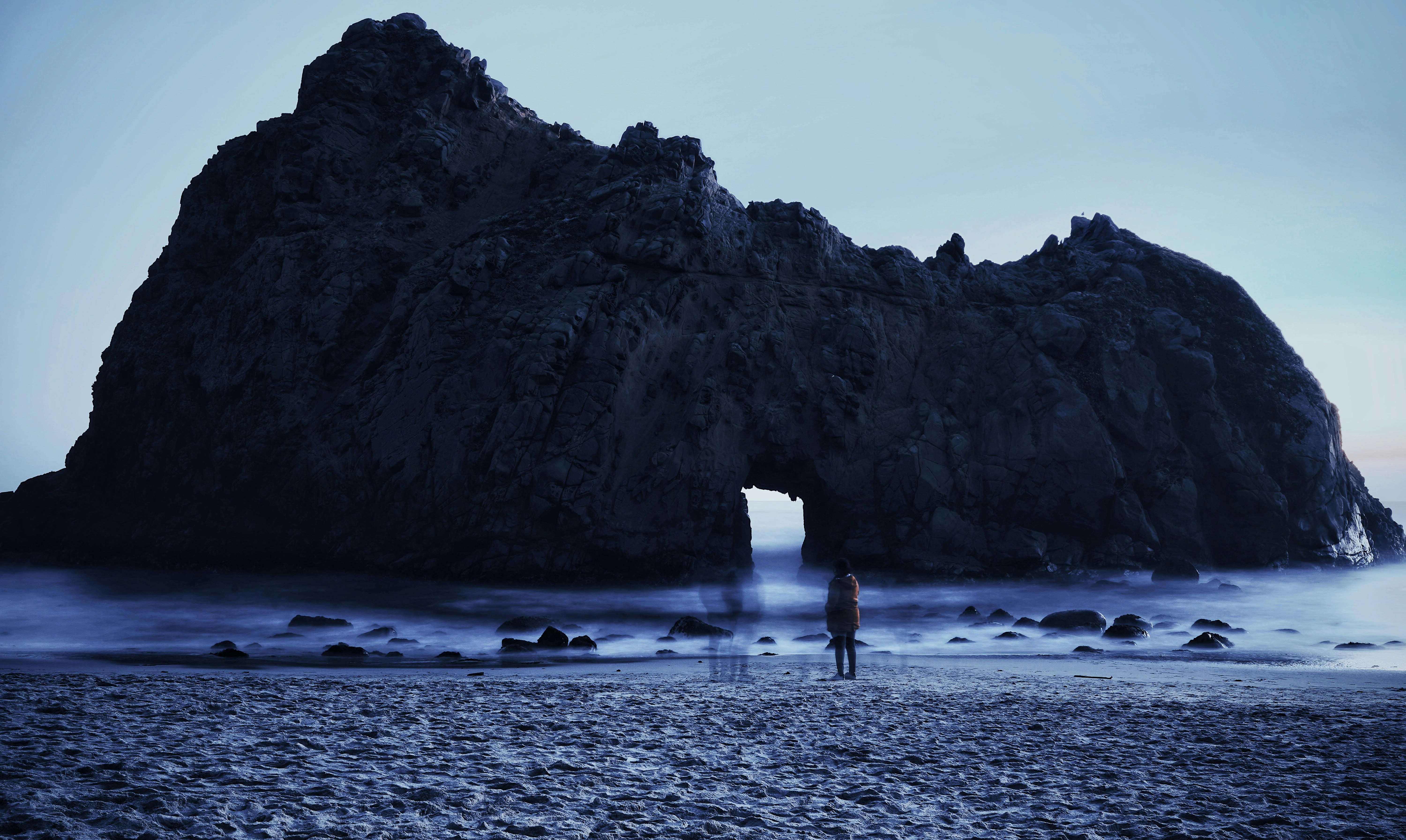 person standing on beach shore near brown rock formation during daytime